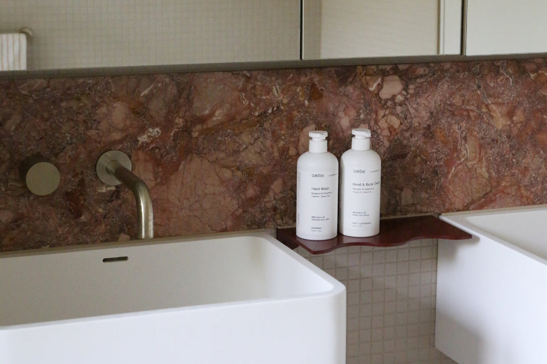 Two sæbe by Designstuff bottles styled on a marble bench in a warm, minimal bathroom with soft lighting and curved sinks.