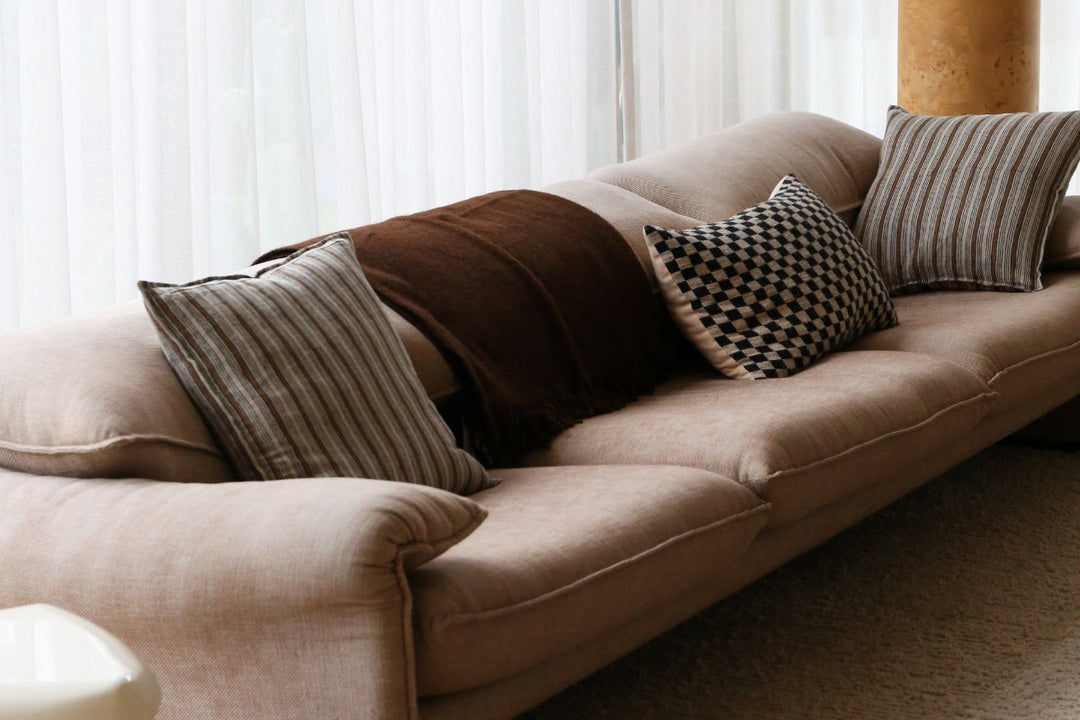 Neutral-toned living room styled with striped and checkered cushions and a warm brown throw on a soft grey sofa.