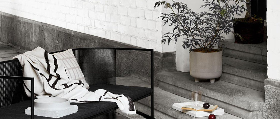 A photo of an outdoor scene featuring a big leafy plant in a Kristina Dam Studio pot next to a Kristina Dam Studio Outdoor Bauhaus Lounge.