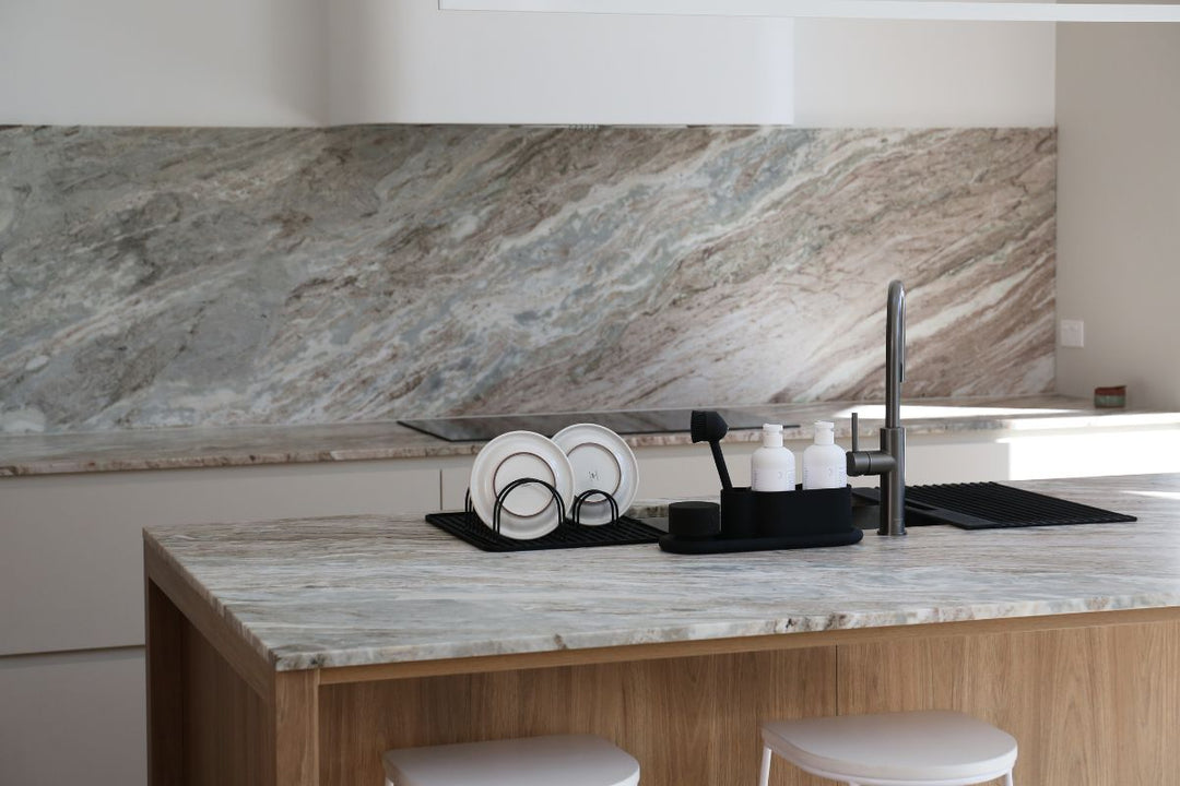Modern kitchen island with a marble benchtop, black dish racks, soap holders and sink accessories arranged beside a black tap.