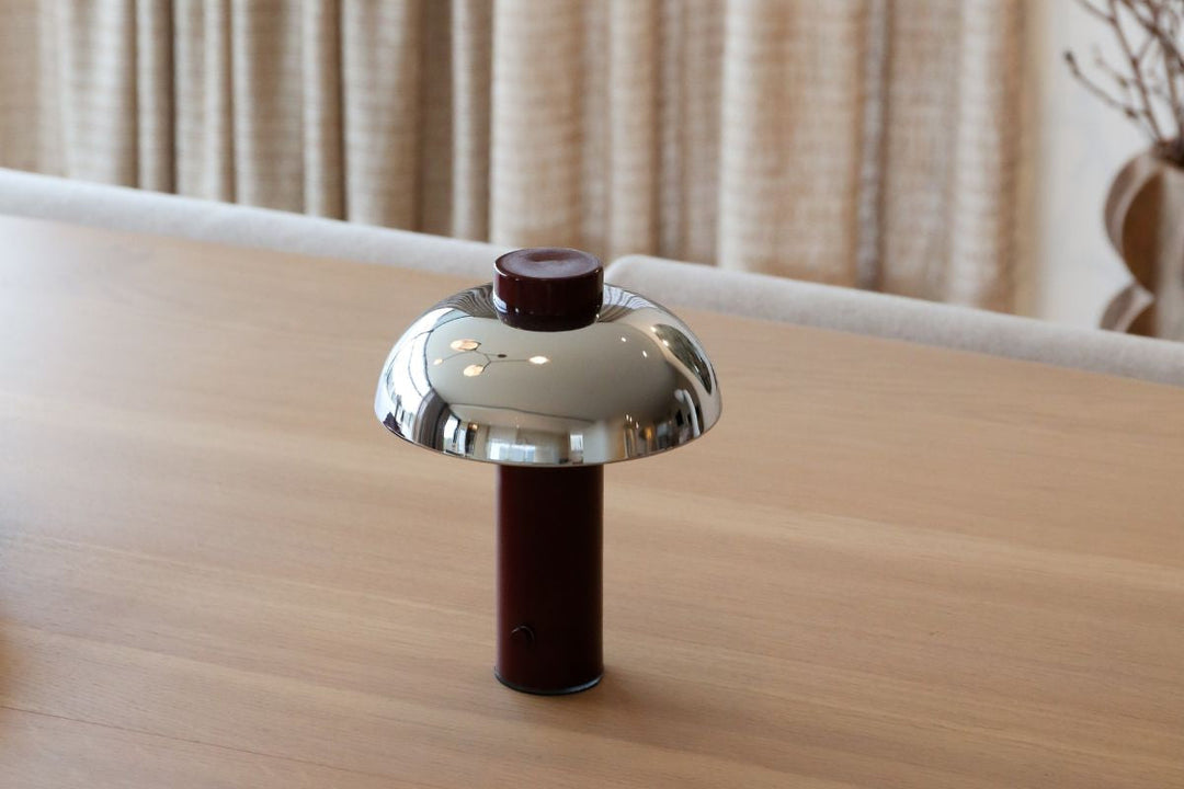 Portable burgundy and chrome table lamp on a timber dining table, with soft curtains and neutral home styling in the background.