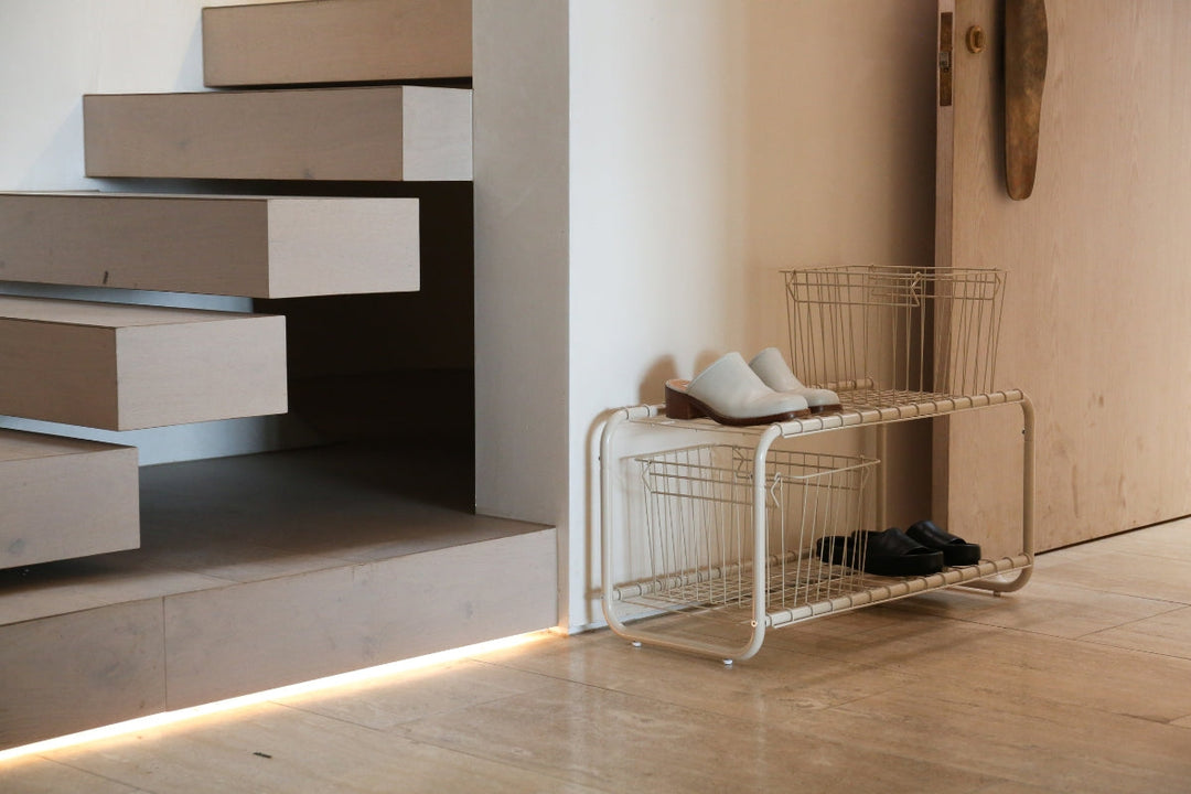 Minimal entryway with floating timber stairs and a low metal shoe rack with wire storage baskets.