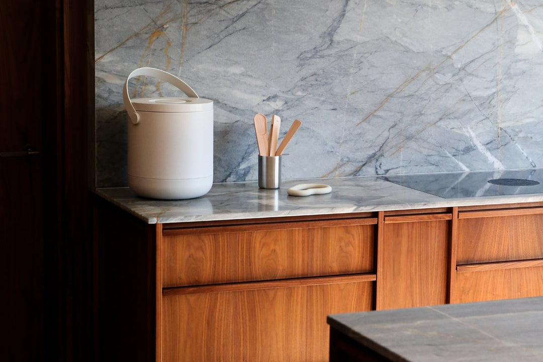 Minimalist kitchen bench with warm timber cabinetry, grey marble splashback, and Zone Denmark bio waste bin in warm grey.