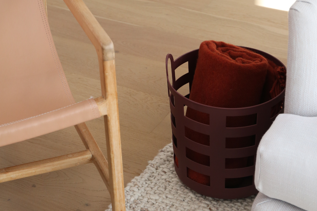 Burgundy storage basket holding folded blankets beside a sofa and timber chair for a 5-minute living room reset.