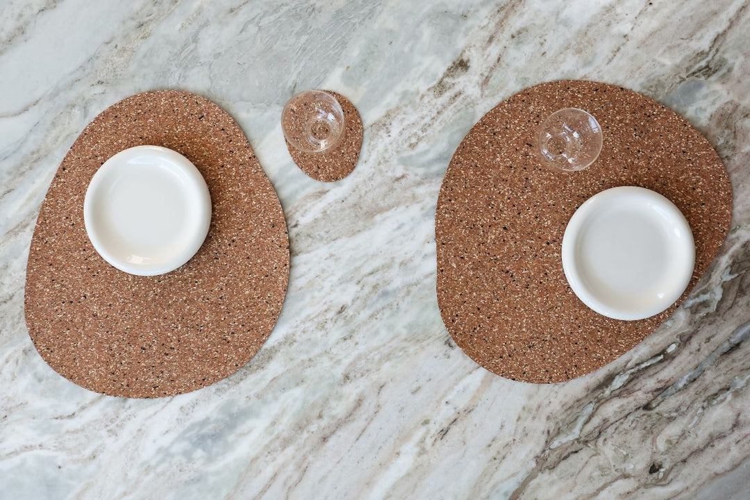 Two freckled placemats styled with white plates and clear glasses on a marble table for relaxed winter hosting.