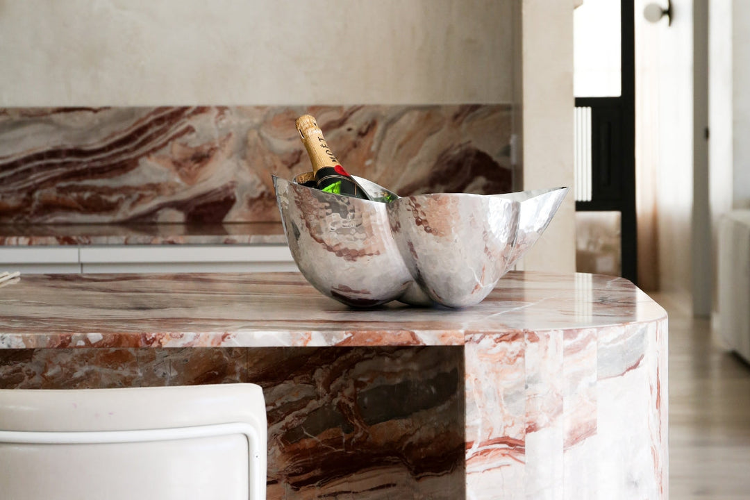 Tom Dixon Cloud Bowl Ice Bucket displayed on a pink marble kitchen counter with champagne bottles inside.