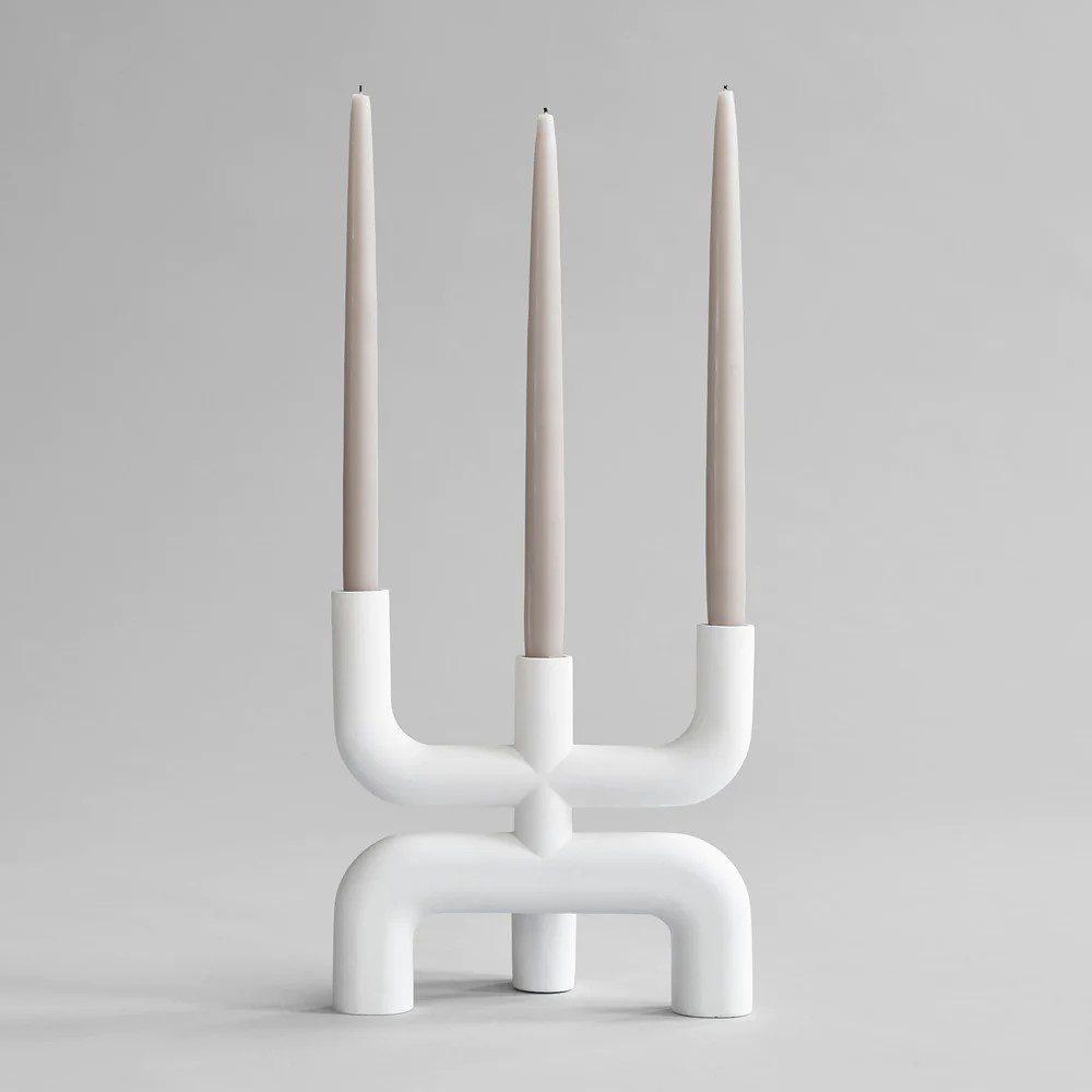 Studio photography of a white three pronged candelabra displayed with three neutral coloured tapered candles