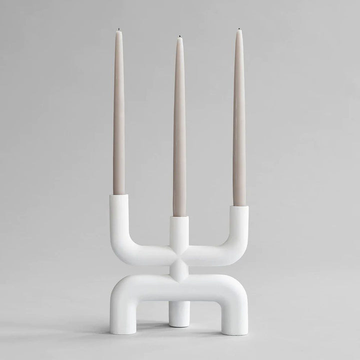 Studio photography of a white three pronged candelabra displayed with three neutral coloured tapered candles