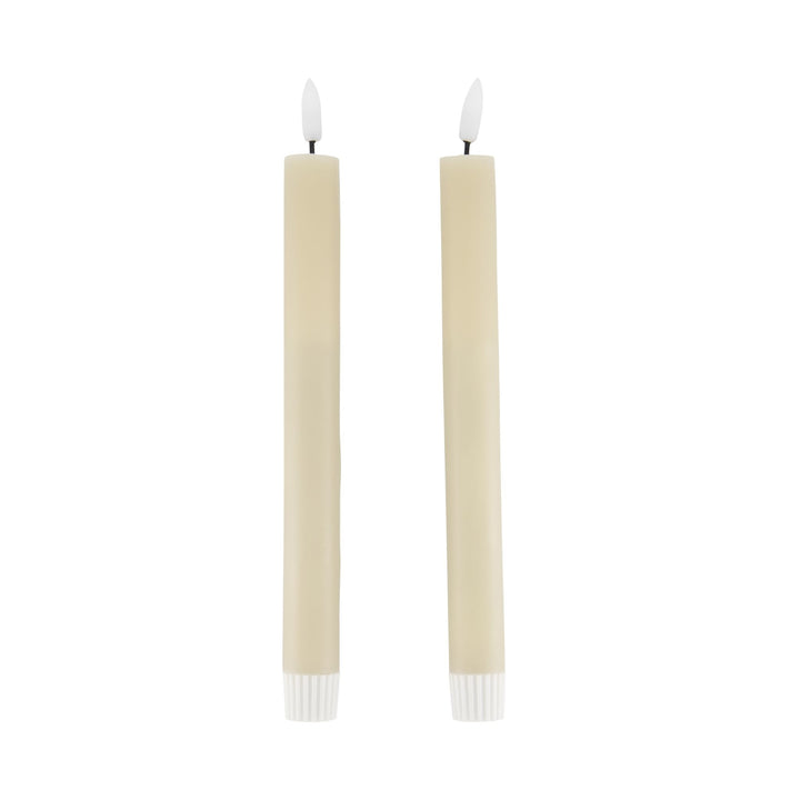 Two beige candles with white wicks on a white background