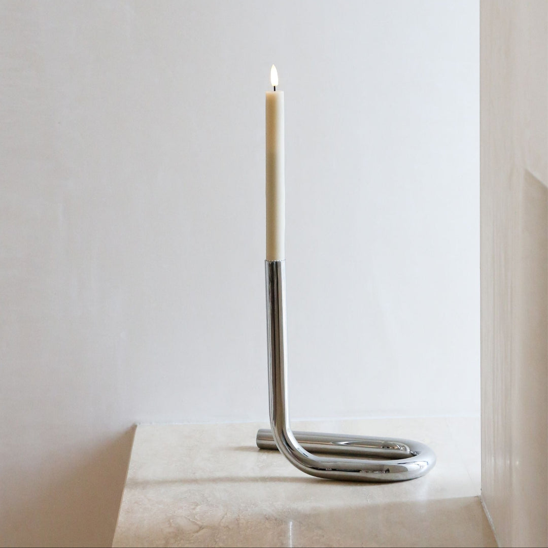 Candle in a modern metal holder on a white surface with a light gray background