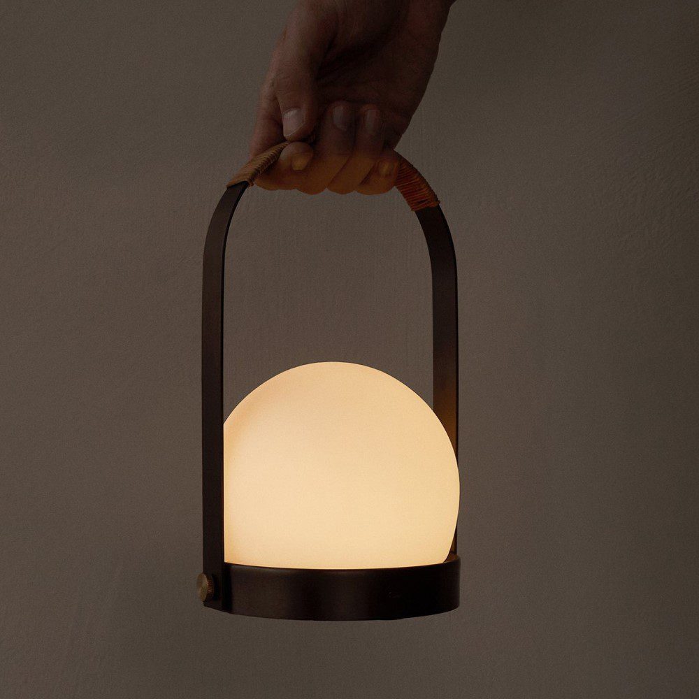 Dimly lit hand carrying a portable round shaped lamp.