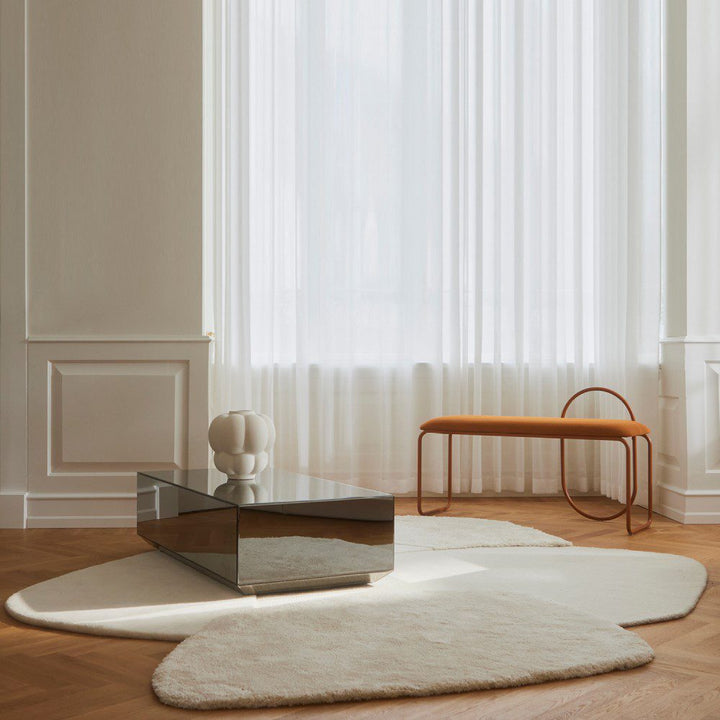 Natural lighting, perspective view of a rug topped with a glass table next to a bench.