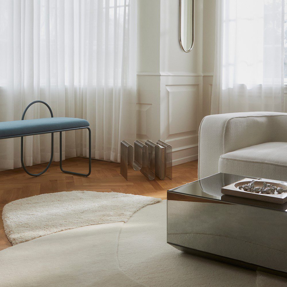 Natural lighting, perspective view of a rug topped with a glass table next to a bench and sofa.