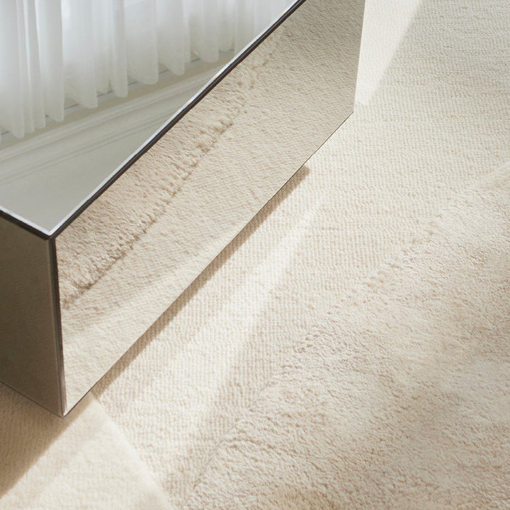 Natural lighting, perspective view of a rug topped with a glass table.