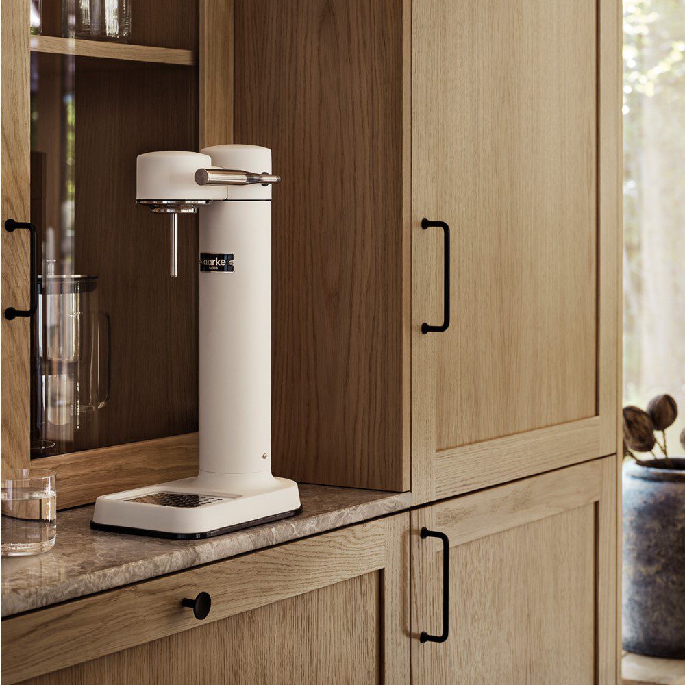 A kitchen cabinet with an empty cylindrical shaped carbonator placed next to a display of glasses.