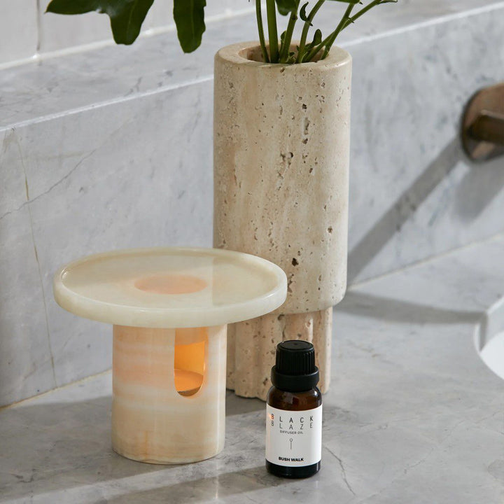 A cylinder-shaped oil diffuser with a round tray on top placed next to an oil bottle and a vase.