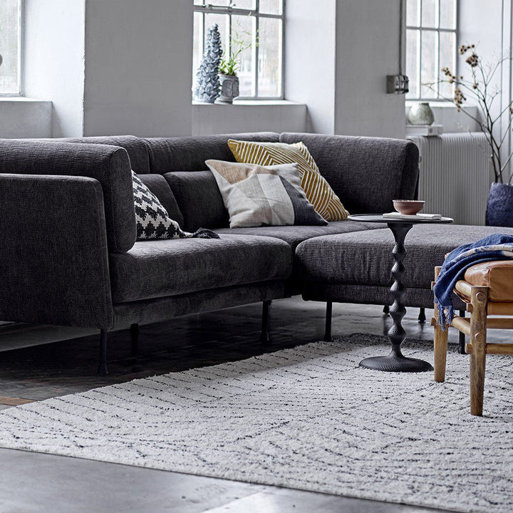 Perspective view of a pillow-filled sofa inside a modern home with a side table placed on the middle of a rug.