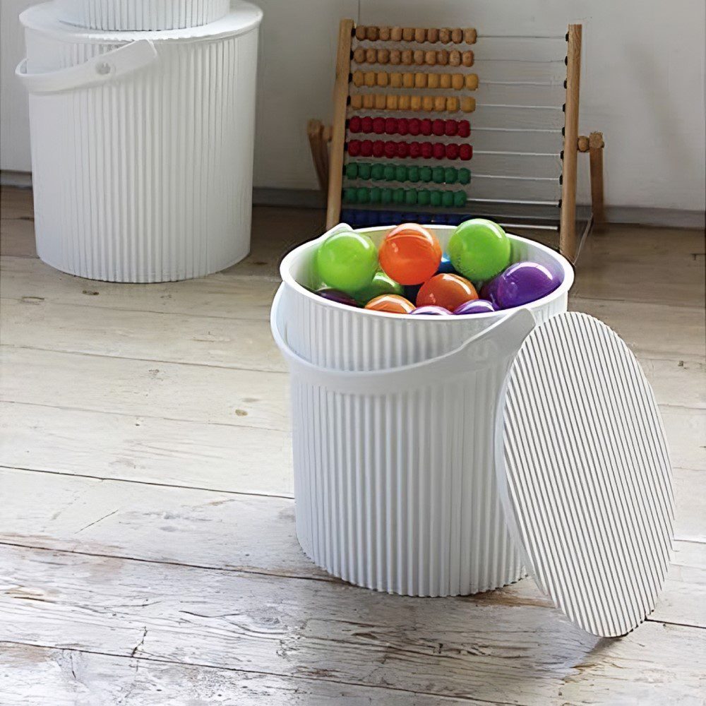 Natural light, perspective view of a white storage bin with multi-coloured balls inside of it and two white storage bins stacked in the background.