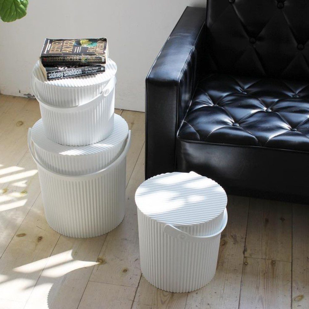 Natural light, perspective photo of a cropped black couch, 3 white and different sized storage bins with one stacked on top of a bigger bin and another one stands on its own.