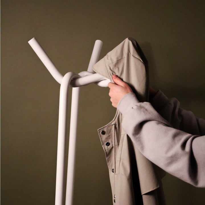 Close up of a person's hand placing a coat on a steel coat rack in a twisted and knitted pattern.