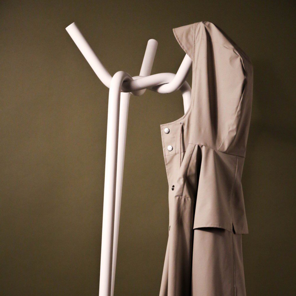 A steel coat rack in a knitted pattern with a coat hung on one of its tips.