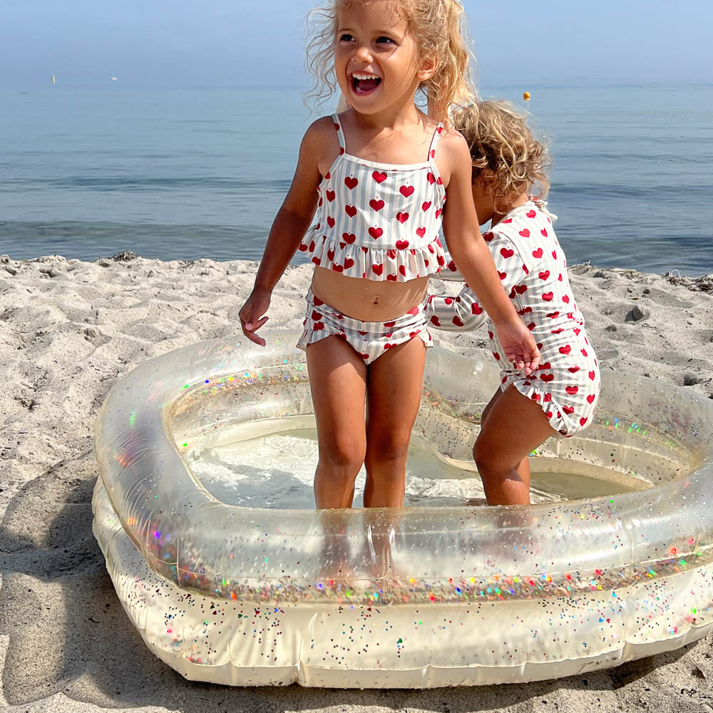 Two kids are playing in the heart shaped kids indoor and outdoor pool with glitter and confetti at the beach.