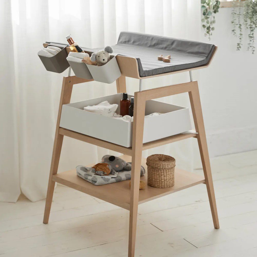 Natural light, perspective view of a wooden baby changing stand with 3 grey organisers attached to its side.