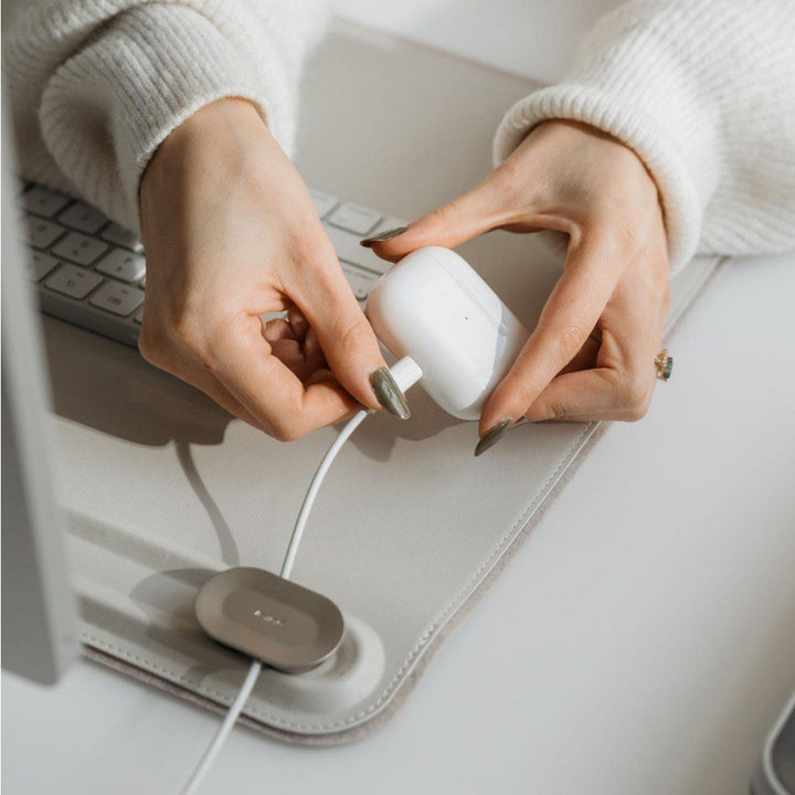 Close up shot of a person pulling a headphone charging case off its wire attached to a rectangular leather desk mat.