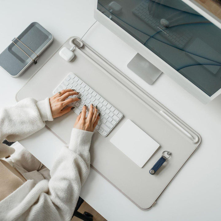 Natural lighting, top view of person typing on a keyboard placed on top of a rectangular-shaped, light grey desk mat.