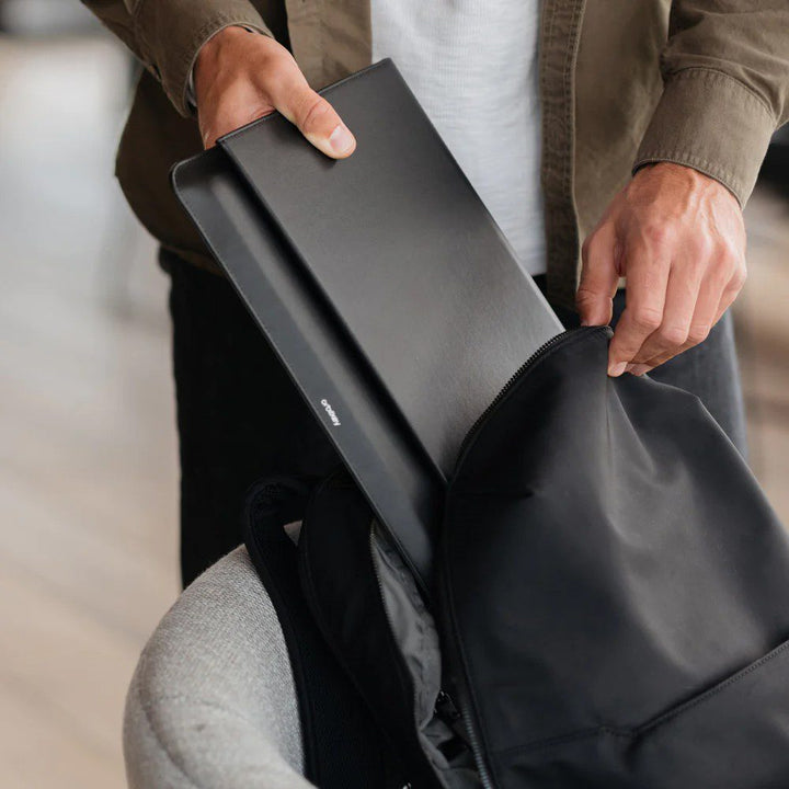 A person storing their hybrid laptop sleeve and desk mat inside a backpack.