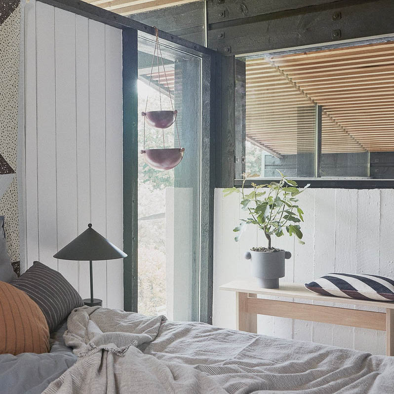 Kotai bench made from oak in a bedroom with a flower pot and a cushion.