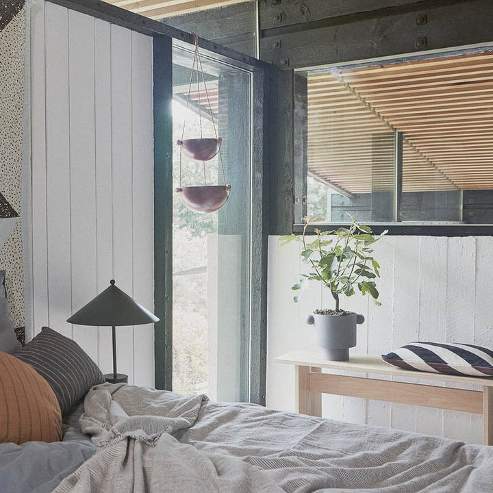 Kotai bench made from oak in a bedroom with a flower pot and a cushion.