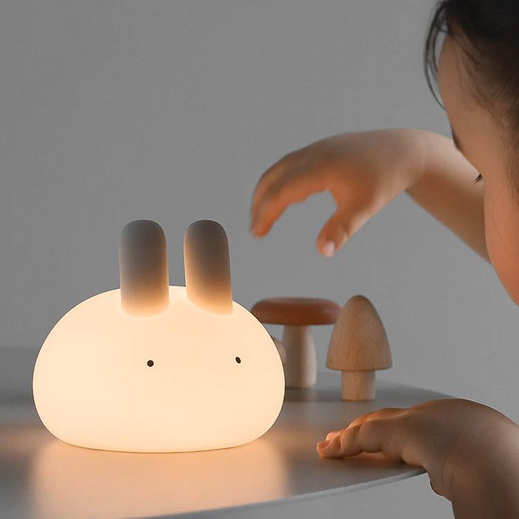 A toddle is grabbing Bunny night lamp on the table.