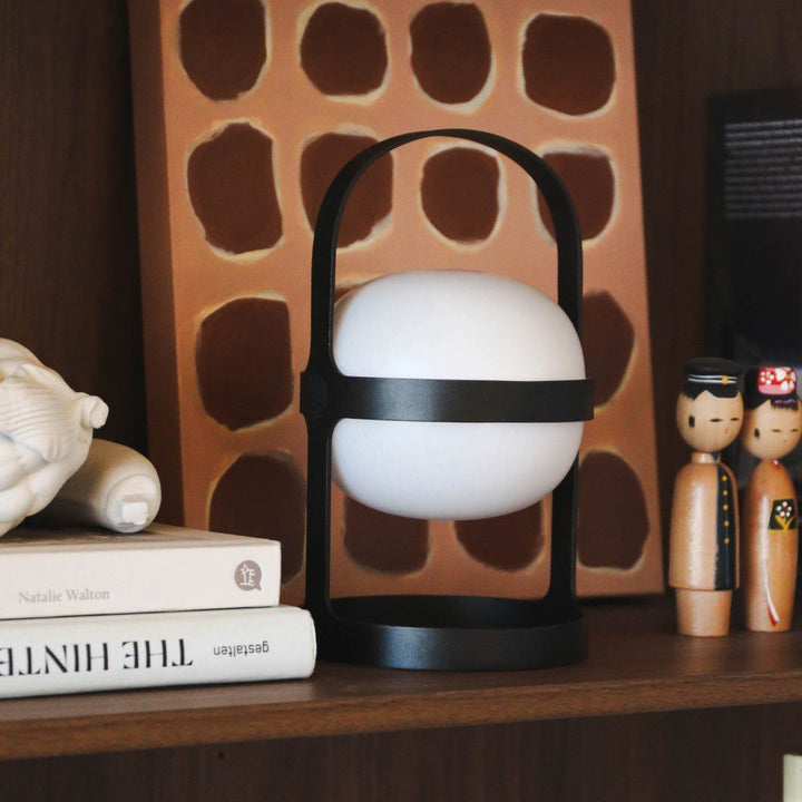 A spherical shaped lamp with a arch-shaped handle placed to a shelf next to books and small objects.