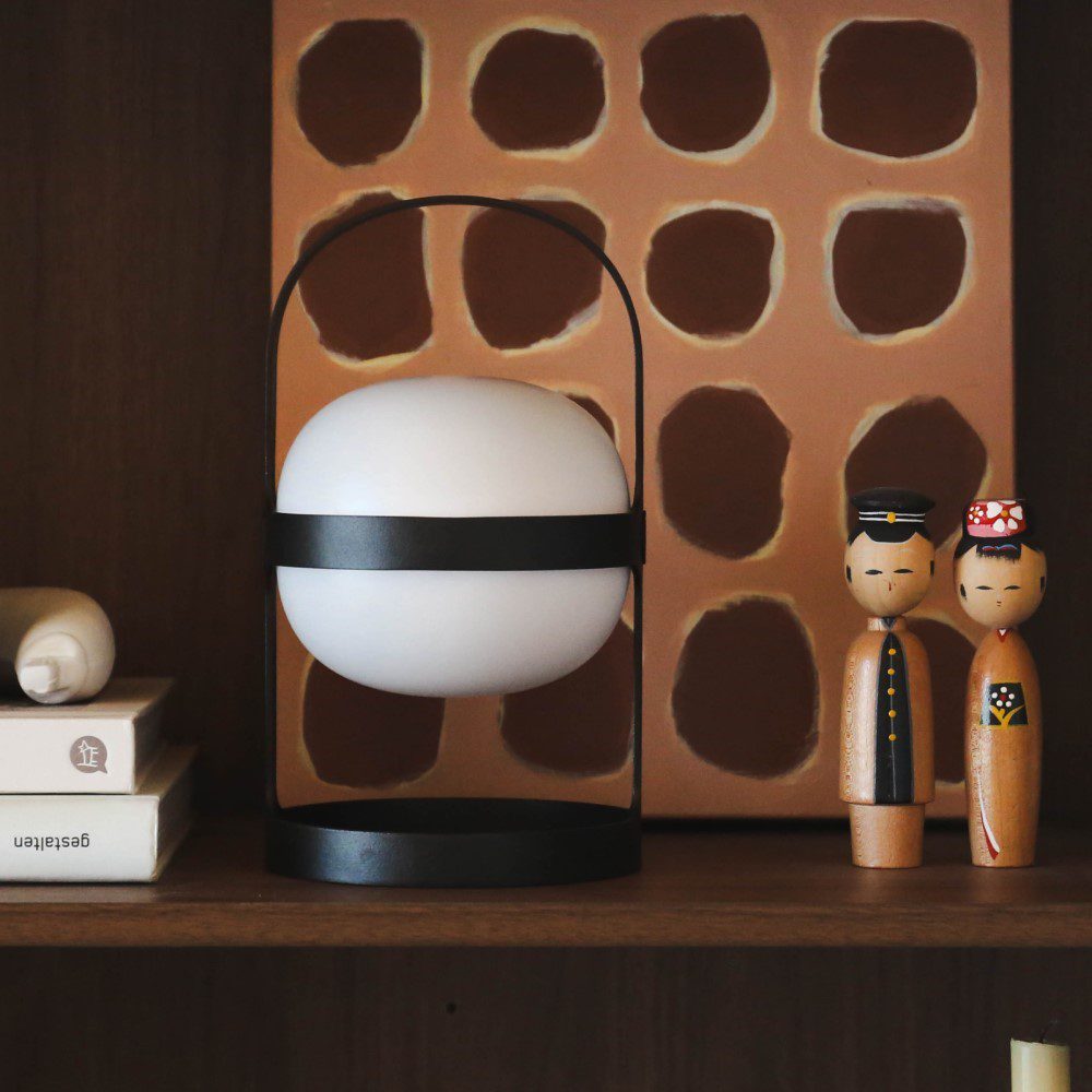 A spherical shaped lamp with a arch-shaped handle placed to a shelf next to books and small objects.