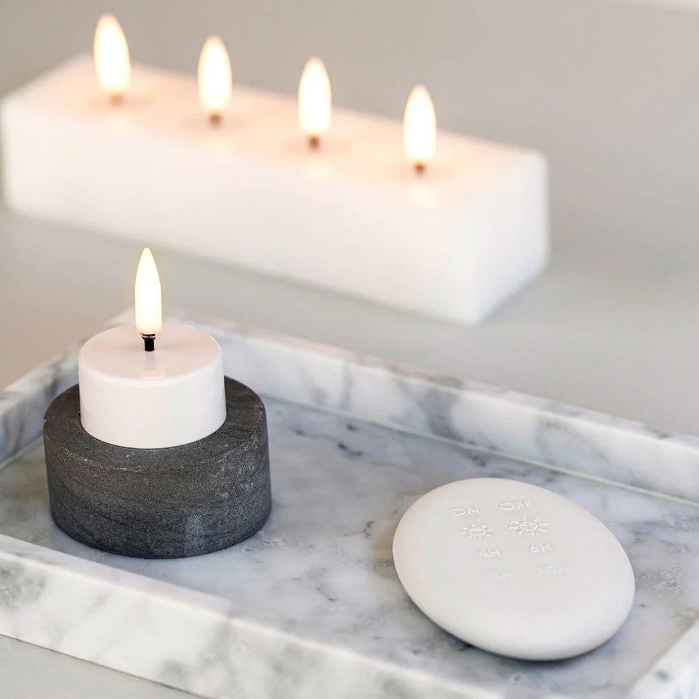 A rectangular-shaped flameless candle next to a remote controller and cylindrical shaped tealight flameless candle.