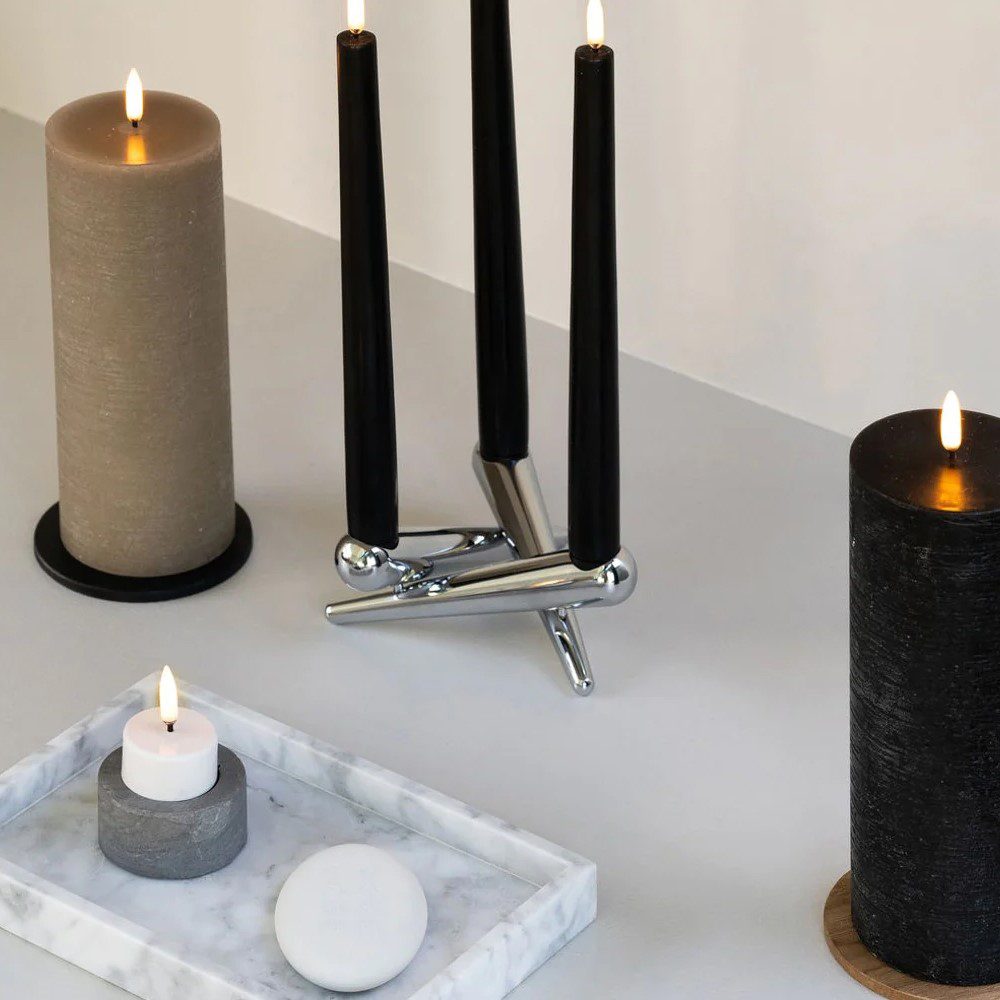 An oval-shaped, flameless candle remote controller placed next to different shaped and sized candles.