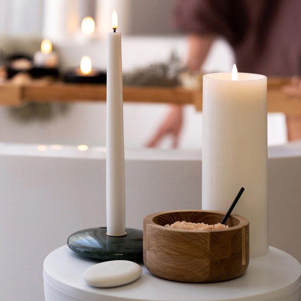 An oval-shaped, flameless candle remote controller placed next to different shaped and sized candles.