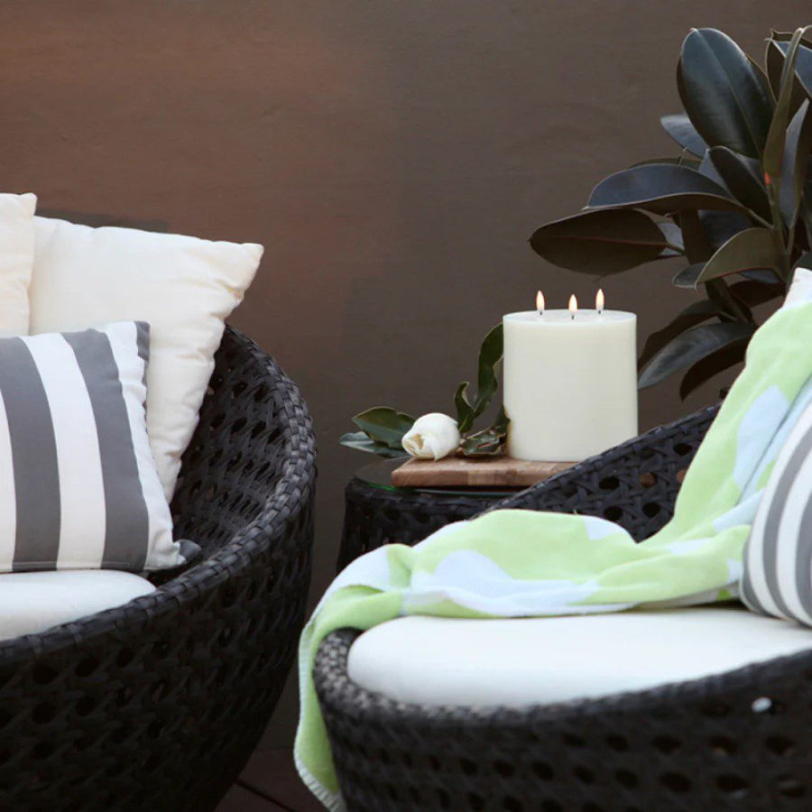 A three-wicked, flameless pillar candle placed on a table between two chairs.