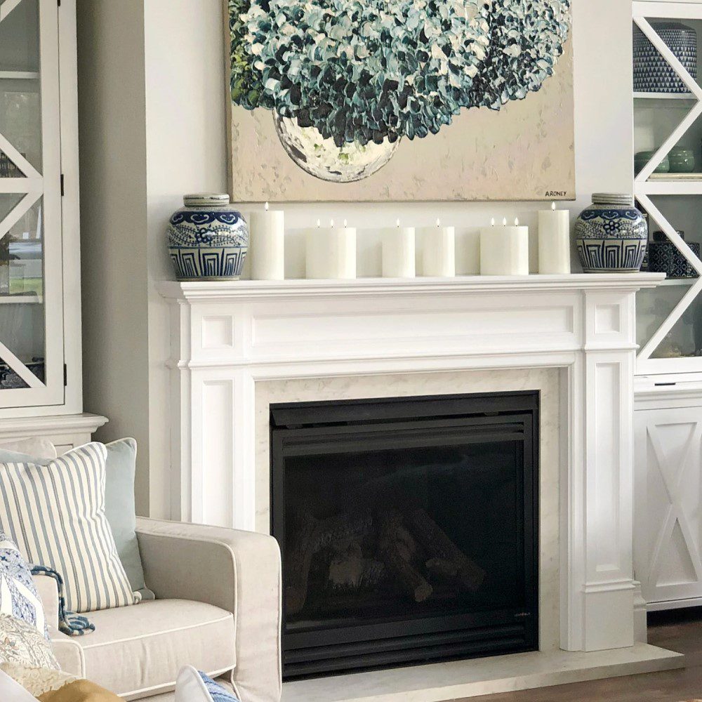 Rows of flameless, pillar candles standing next to each other and placed above a fireplace.