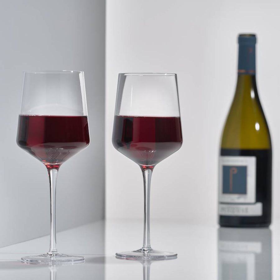 Set of 2 mouth-blown Rocks red wine glasses by Zone Denmark and a bottle of wine.