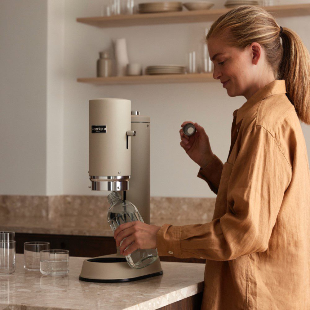 A person in a kitchen placing a glass bottle inside a cannister-shaped water carbonator