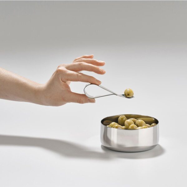 A cropped image of a hand taking an olive away from a silver bowl using a teardrop-shaped silver spoon.
